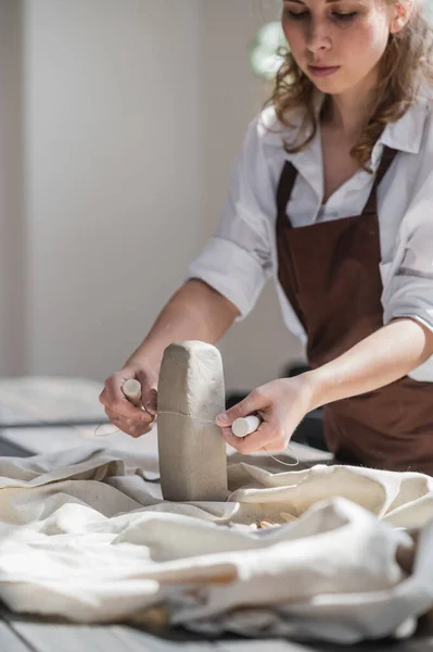 女性の陶芸家は、トリミングツールのクローズアップを使用して陶器の粘土の作品を切断。女性は粘土カッターを粘土の生の部分に使用する — ストック写真