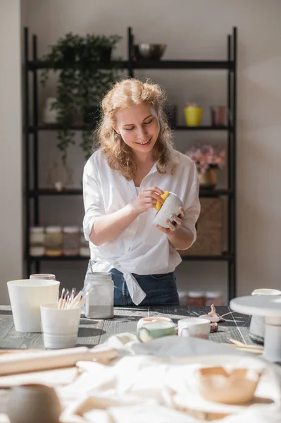 Mujer joven en el estudio de cerámica limpiar pintura esmalte innecesario con una esponja . — Foto de Stock
