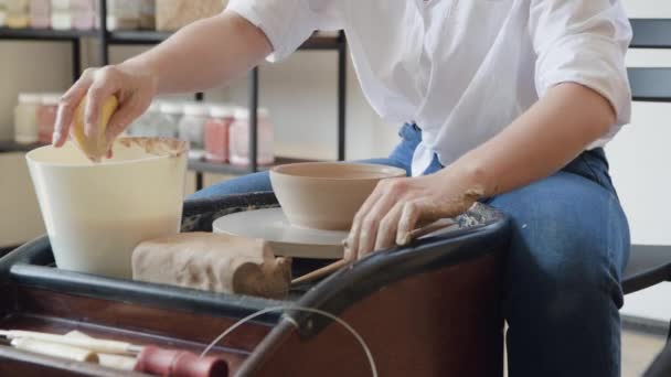 Alfarero femenino trabajando con arcilla sobre ruedas en estudio. Arcilla con agua salpicada alrededor de la rueda de alfarero. — Vídeos de Stock