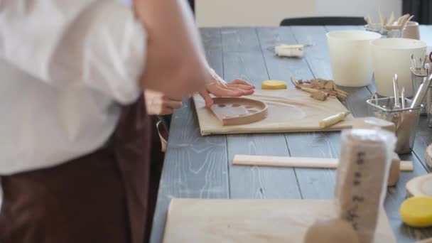 Женские руки держат палку и делают орнамент на декоративном продукте. глина мастер формования глины на керамической мастерской. — стоковое видео