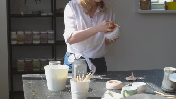 Jonge vrouw in aardewerk studio vegen onnodige glazuur verf met een spons. — Stockvideo