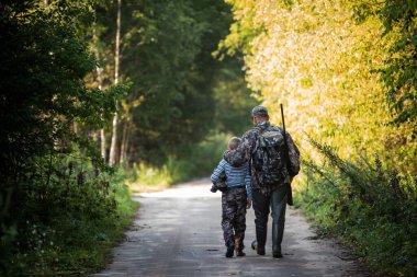 Baba ve oğul birlikte avlanıyorlar. Kuş avından sonra yolda yürürken.