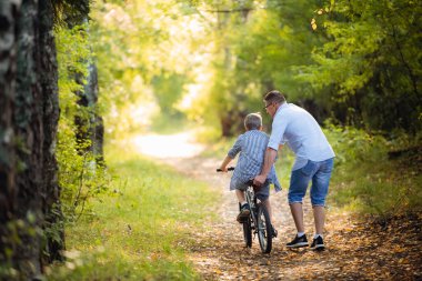 Baba oğluna bisiklet sürmeyi öğretiyor.