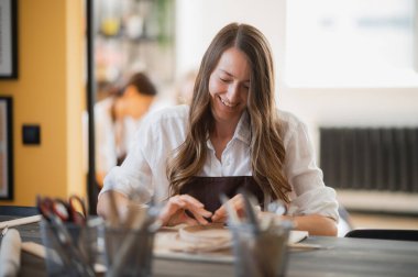 Çömlekçilik sınıfındaki genç bir kadın farklı aletlerle çalışıyor..