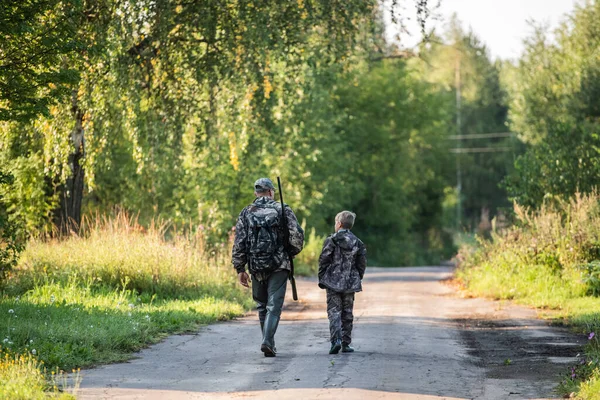 Pai e filho caçam juntos. Caminhando pela estrada depois da caça ao pássaro . — Fotografia de Stock