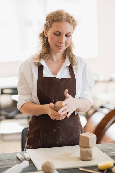 Женщина-гончар, формирующая кусок глины за столом. Женщина делает керамические изделия. Керамика, ручная работа и творческие навыки в художественной студии.