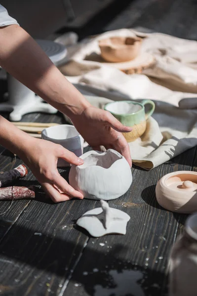 Жіночі руки обережно кладуть готову глазуровану чашу на дерев'яний стіл з різними керамічними інструментами . — стокове фото