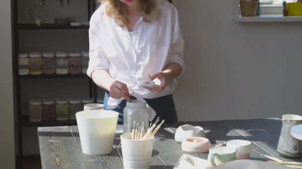 Девушка рисует на глиняной чаше. Женщина гончар работает в своей студии остекление керамический горшок. — стоковое видео