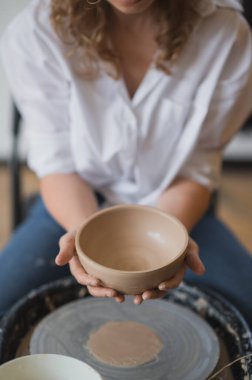 Çömlekçi çarkında çalışan bir kadın kendi elleriyle bulaşık yapıyor. Kirli ellerin çamuru şekillendirdiği yakın plan fotoğraf.