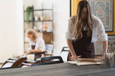Kadın eli, seramik stüdyodaki ahşap merdaneyle kumaş parçalarını düzleştiriyor..