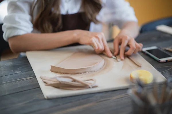 Oleiro fêmea artesanal prepara material para sua cerâmica. As mãos de mulher anexam a parte de barro ao futuro produto cerâmico. Plano de trabalho. — Fotografia de Stock