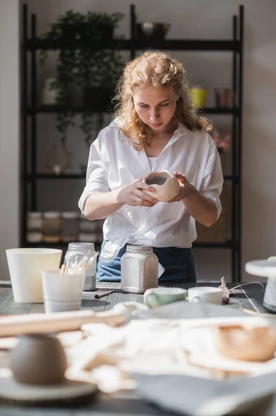 Femme potier assis et remuant peindre avec un pinceau une tasse sur la table. Femme fabriquant des articles en céramique. Poterie, savoir-faire artisanal et créatif. — Photo