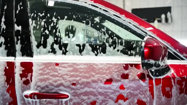 Widok przez boczne okno samochodu na człowieka myjącego mydlaną czerwoną brykę na tle. Koncepcja czyszczenia i szczegółowości. — Wideo stockowe