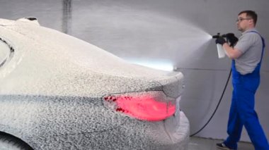 Araba yıkama servisinde duran arka farları açık bir araba. İşçiler arabayı yüksek basınçlı spreyle kaplıyorlar..