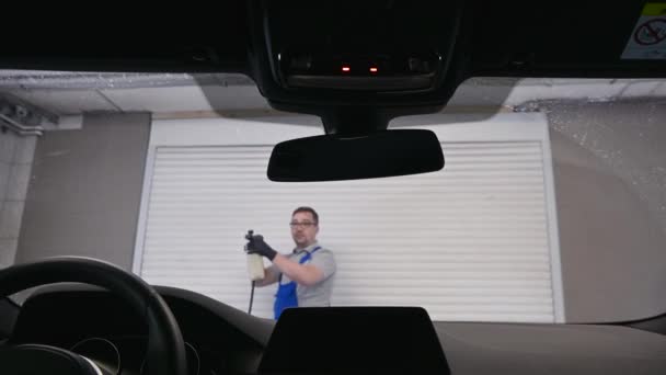 Trabalhador na loja de lavagem de carros jogando sabão na janela do carro. Vista de dentro do carro . — Vídeo de Stock