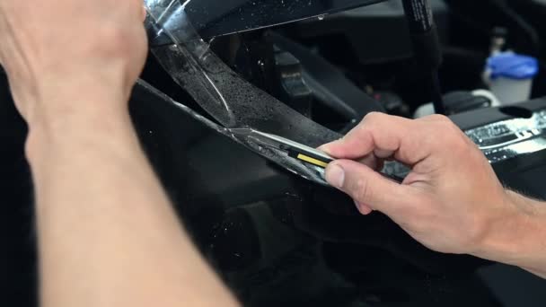 男の専門家は、自動車サービスのハンドルのための車の体に保護ビニールの鞘を切断している — ストック動画