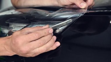 Ustanın özel bıçakla vinil film keserken yakın plan çekimi. Uzman, araba yüzeyindeki filmleri birleştirmek için düzgün bir kesik attı.