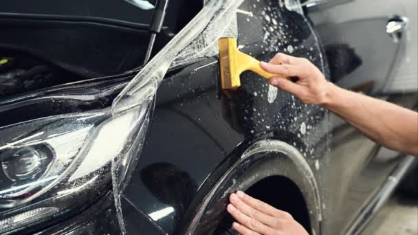 Primer plano de las manos del hombre que desengancha la película con la capucha negra de un coche. Esta película protege al vehículo de los daños . — Vídeos de Stock