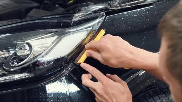 Film de protection contre la peinture Installation sur une voiture noire. Master applique un film protecteur en polyuréthane à l'aide d'un outil raclette pour éliminer l'excès d'eau sous la surface du film. — Video