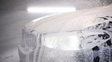 Beyaz kar köpüğü şampuanıyla temizlik arabası. Arabanın kaputuna ve farına beyaz kar köpüğü serpiyor. Araba şampuanı araba kaputuna köpük sıkıyor.