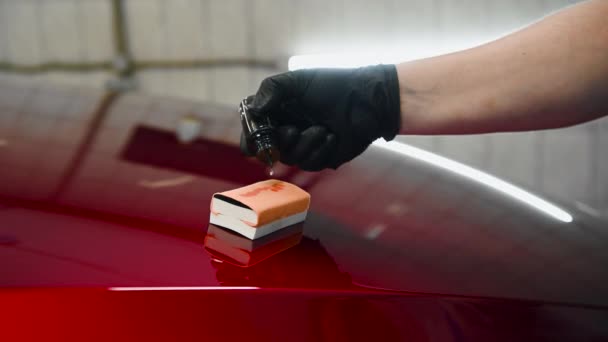 Primo piano di un uomo mano gocciolante rivestimento liquido su un applicatore spugna su un cofano auto. Preparazione per l'applicazione di un rivestimento speciale su una superficie dell'auto. — Video Stock