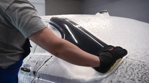 Крупним планом чоловіча рука в чорній рукавичці з піною для миття даху автомобіля. Концепція: автосервіс, автомийка , — стокове відео