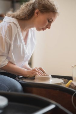 Çömlekçi çarkında çalışan bir kadın kendi elleriyle bulaşık yapıyor. Kirli ellerin çamuru şekillendirdiği yakın plan fotoğraf.