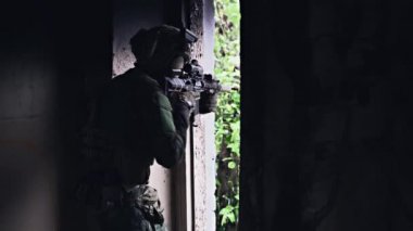 Askeri asker elinde bir saldırı tüfeği tutuyor, köşedeki olası düşmanları kontrol ediyor.