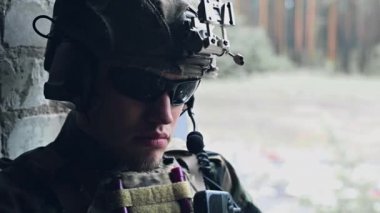 Gözlüklü asker portresi, ordu miğferi ve telsiz oturup etrafa bakınıyordu. Askerle yüzleşin.