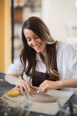 Çömlekçilik sınıfındaki genç bir kadın farklı aletlerle çalışıyor..