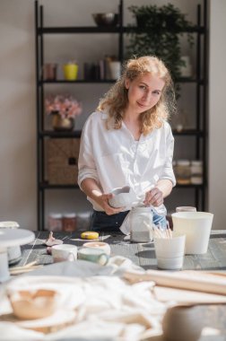 Dişi çömlekçi fırça kullanarak çiğ seramik bardak parlatıyor. Çömlek atölyesine rengarenk koyan çömlek kupası.