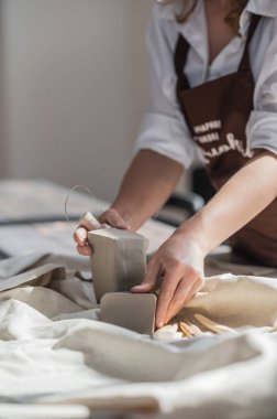 Kadın çömlekçi yakın çekim aracı kullanarak çömlek kil kesiyor. Kadın kil kesiciyi ham bir kil parçası için kullanıyor.