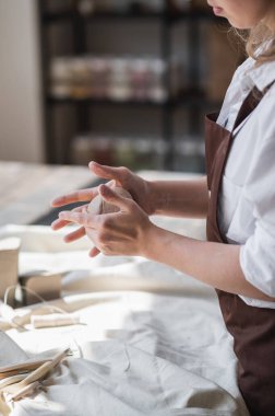 Bir kadın çömlekçi, atölyedeki ahşap bir masanın arka planına kahverengi bir çömlek yontuyor.