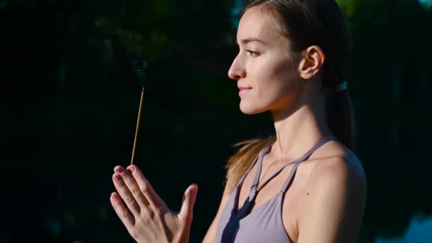 Yoga yapan ve güneşin doğuşunda meditasyon yapan bir kadın ellerinde aroma çubuğu, ellerinde namaste jesti olan bir kadın.. — Stok video