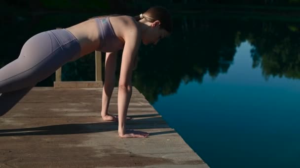 Młoda, atrakcyjna dziewczyna ćwiczy jogę nad jeziorem o zachodzie słońca. Siedzenie w pozycji lotosu nad wodą. — Wideo stockowe