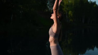 Güneşli bir günde, bir orman gölünde ruhani yoga pozu veren güzel genç bir kadın.