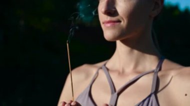 Yoga yapan ve güneşin doğuşunda meditasyon yapan bir kadın ellerinde aroma çubuğu, ellerinde namaste jesti olan bir kadın..