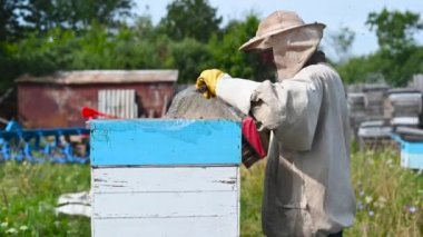 Eko apikültür ve bal üretim işi. Arı yetiştiricisi arıları arıların evlerinden bal peteğini temizlemek için dumanla dezenfekte ediyor. Beepeekleme işlemi.