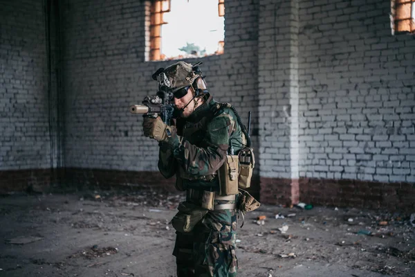 Στρατιωτικός στρατιώτης με τη μορφή κρατά στα χέρια του ένα τουφέκι, ελέγχει πιθανούς εχθρούς γύρω από τη γωνία — Φωτογραφία Αρχείου