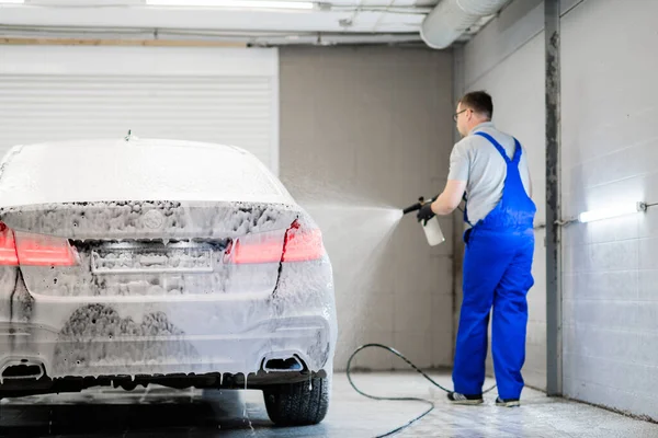 Cleaning car with white snow foam shampoo. Spraying white snow foam on a car. Spraying car shampoo foam to car.