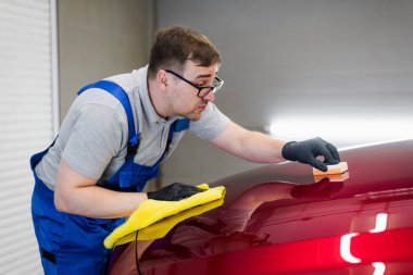 Stüdyoda çalışan adam araba boyasına sünger aplikatörüyle seramik kaplama uyguluyor.