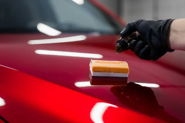 車の詳細-人間は赤い車のナノ保護コーティングまたはワックスを適用します。液状のガラス研磨剤で車のボンネットを覆う. — ストック写真