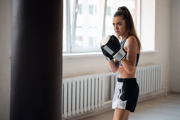Dívka se připravuje na boxerskou soutěž a trénuje údery na boxovací pytel v prostorné tělocvičně — Stock fotografie