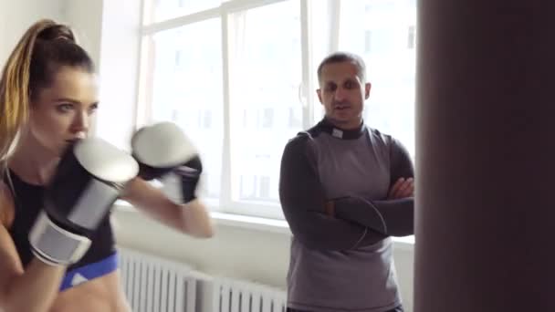 Ein strenger Trainer beobachtet seine Kickboxerin dabei, wie sie in einem geräumigen Trainingsraum einen Schlag auf einen Boxsack übt — Stockvideo