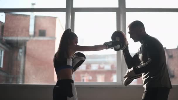 Молодая девушка проводит тренировки по кикбоксингу и практикует удары лапами с профессиональным боксером — стоковое видео