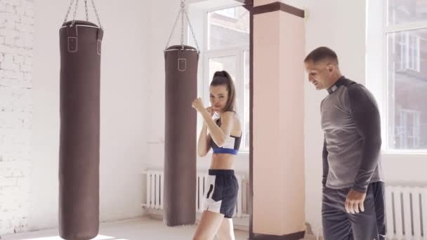 W sali bokserskiej doświadczony trener uczy młodą dziewczynę właściwej postawy. — Wideo stockowe