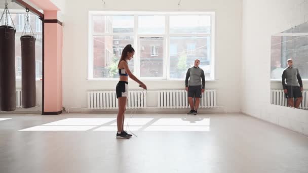 Calienta antes de la sesión de entrenamiento principal, la chica salta con una cuerda, el entrenador observa — Vídeo de stock