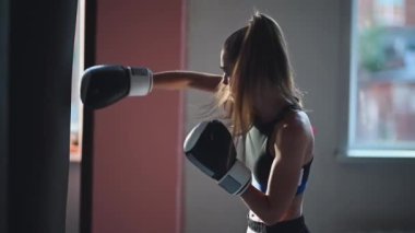 Bir kızın boks müsabakasına hazırlanması ve geniş bir spor salonunda kum torbasına yumruk atması.