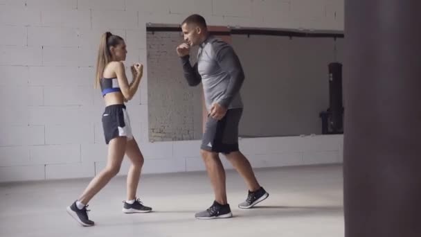 In een ruime hok geven een mannelijke trainer en zijn vrouwelijke mentee een bokstraining — Stockvideo