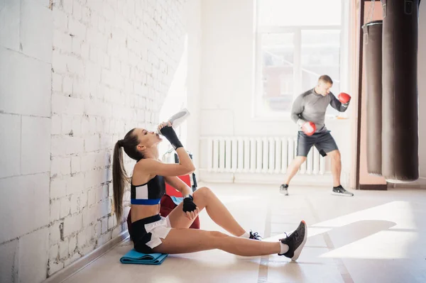 Durante una pausa nell'allenamento di kickboxing, una giovane ragazza carina siede accanto a un muro e beve acqua. — Foto Stock